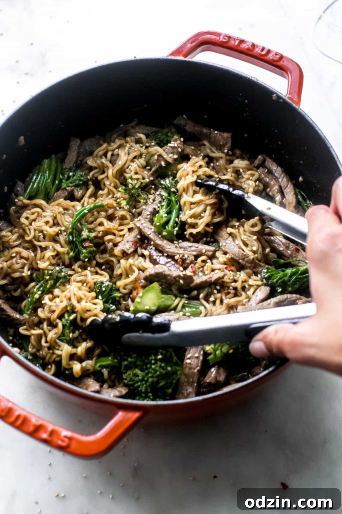 hand using tongs to life broccoli beef ramen from a cast iron pot