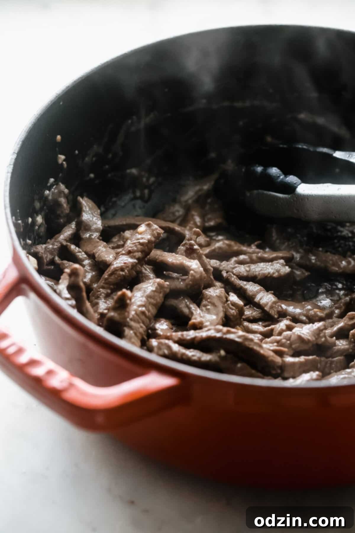 sautéed beef in cast iron pot with tongs