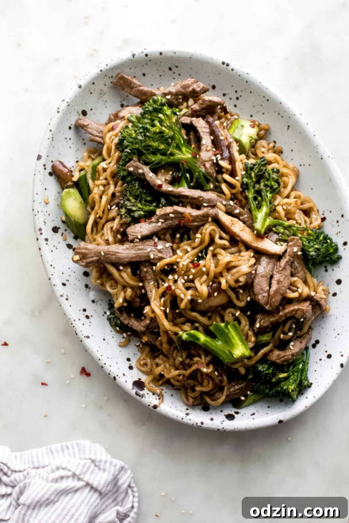 oval speckled plate with ramen noodles that were cooked with broccolini and strips of sautéed beef and mushrooms