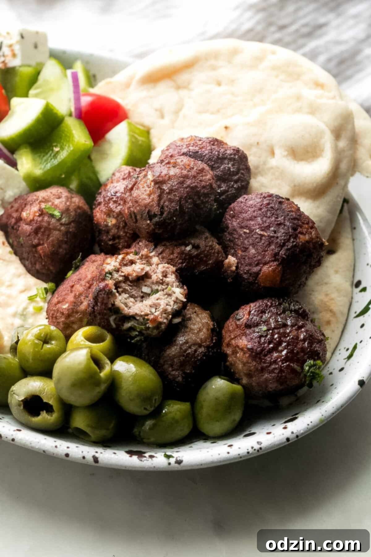 Authentic Greek Keftedes 6 platter of cooked Greek Keftedes meatballs served with pita bread, green olives, Greek salad, and creamy hummus