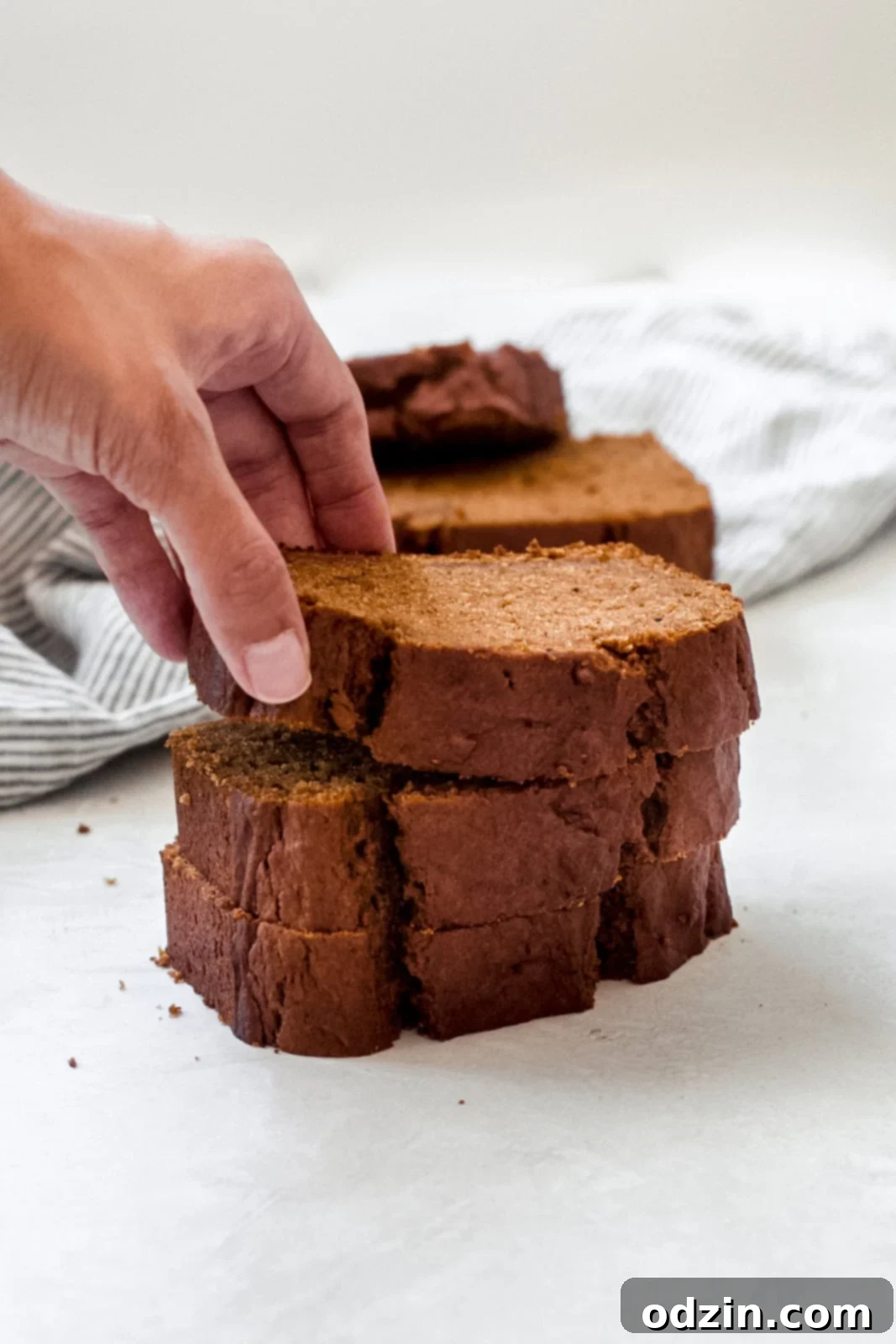 a hand reaching for a thick slice of warm pumpkin bread from a cooling rack