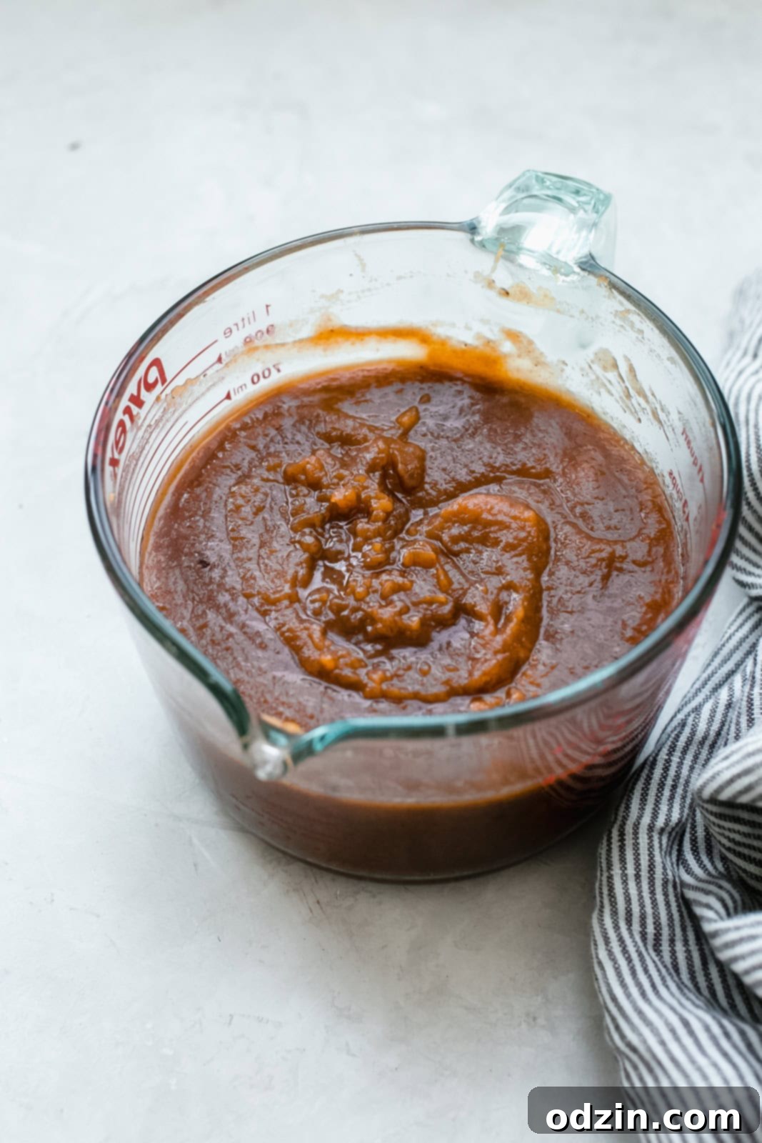 a glass measuring cup filled with a smooth, orange pumpkin mixture, surrounded by various spices