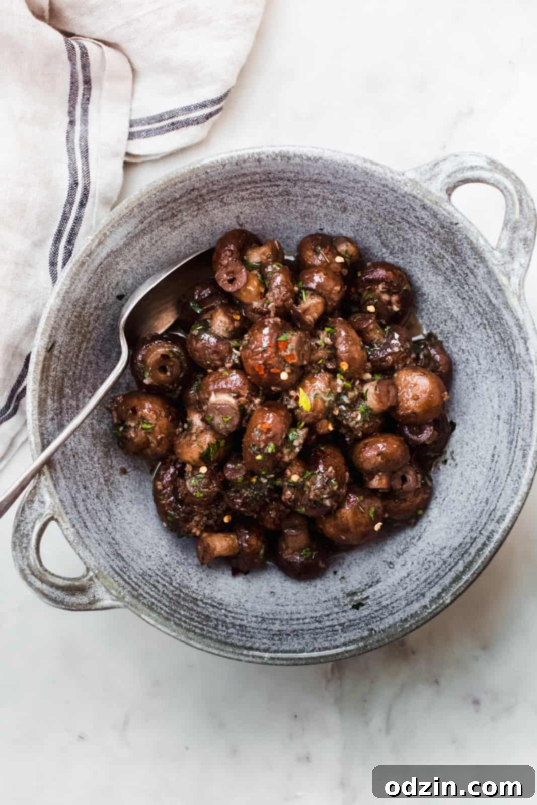 A beautiful bowl of sautéed garlic herb mushrooms presented on a white marble surface, ready to be enjoyed.