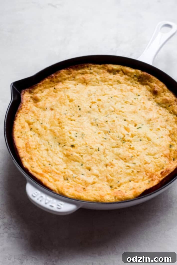 Easy Garlic Cheddar Chive Spoonbread - a simple, cheesy side for Thanksgiving and Christmas Golden brown garlic cheddar chive spoonbread baked in a cast-iron skillet, garnished with fresh chives, perfect for holiday meals.
