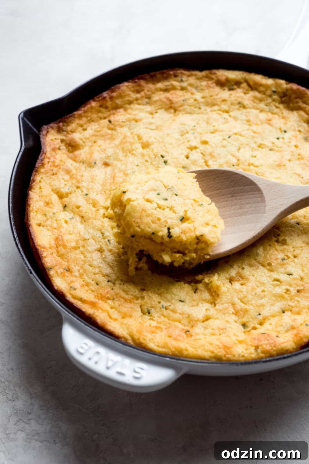 Cheesy Garlic Chive Corn Pudding 2 A wooden spoon scooping a portion of golden, fluffy garlic cheddar chive spoonbread, showing its moist texture.