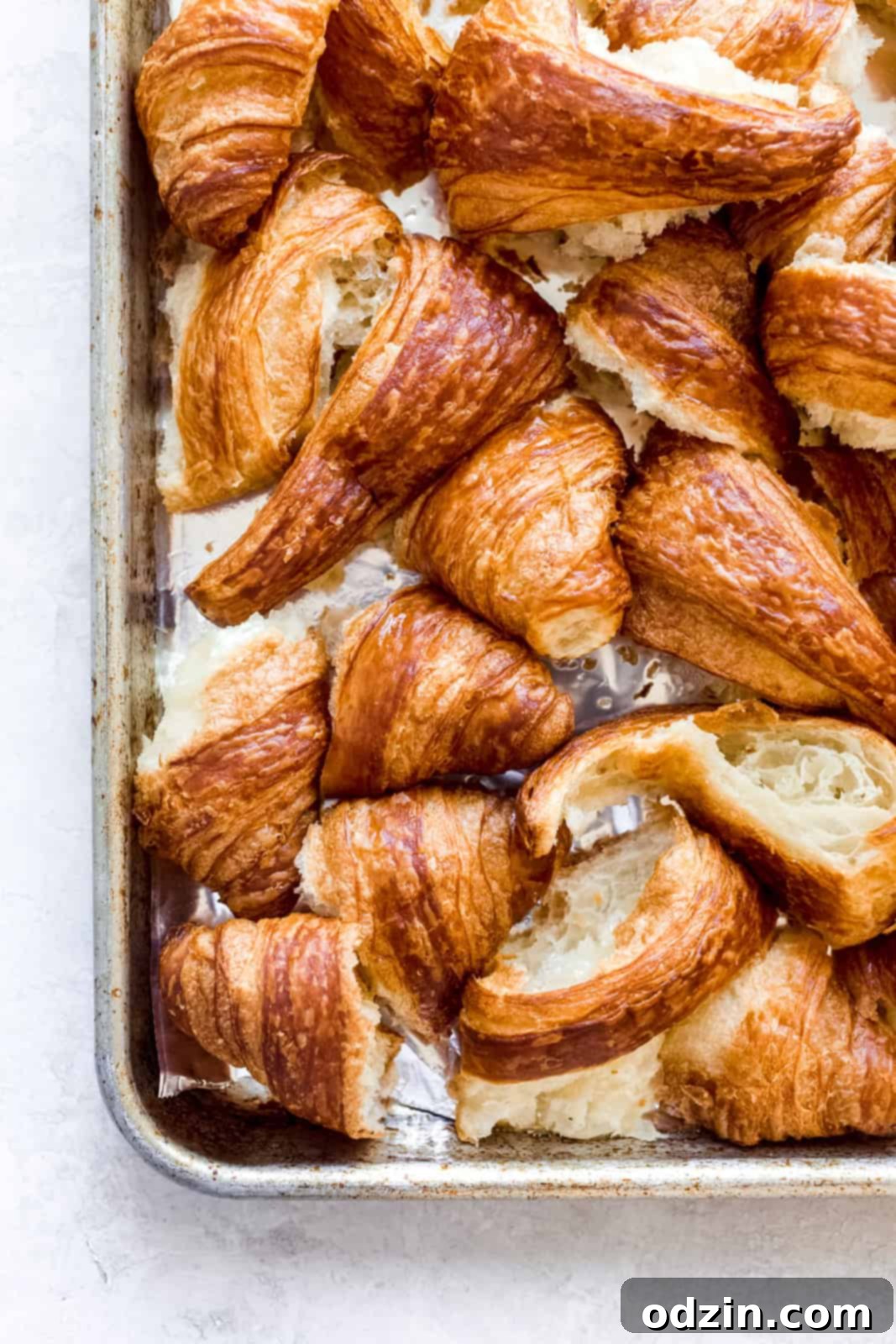Broken croissant pieces arranged on a baking sheet lined with foil, ready for toasting.
