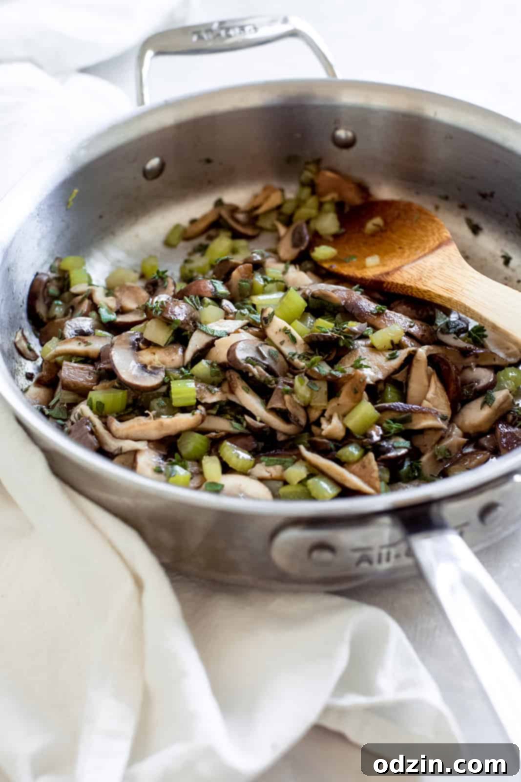 Sautéing diced celery and mushrooms with fresh herbs in a stainless steel pan.