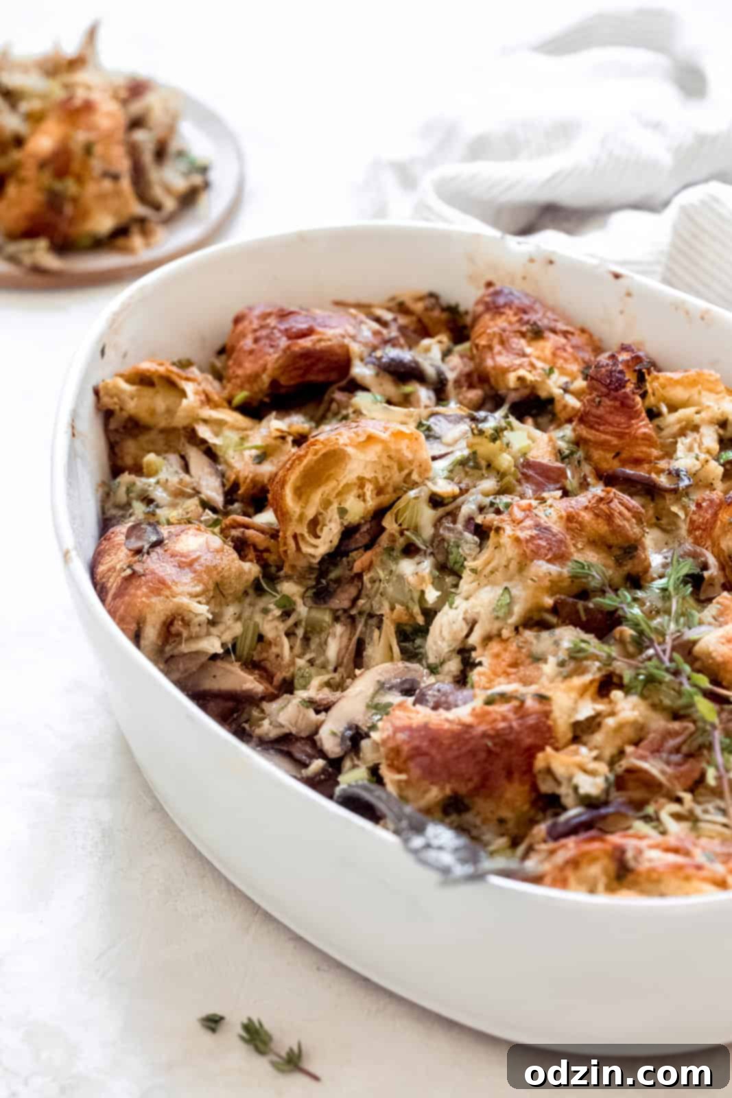 Side view of fluffy, golden-brown croissant stuffing with caramelized onions in a white oval bowl.
