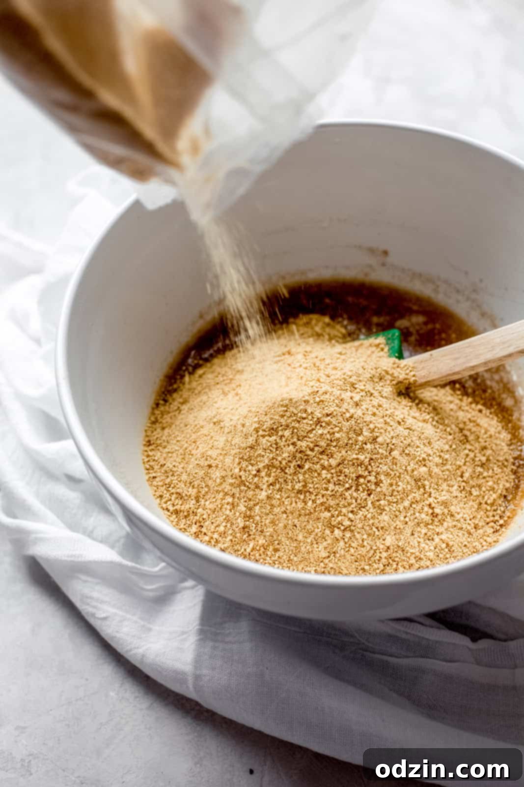 Pouring graham cracker crumbs into a white mixing bowl, ready to be combined for the crust