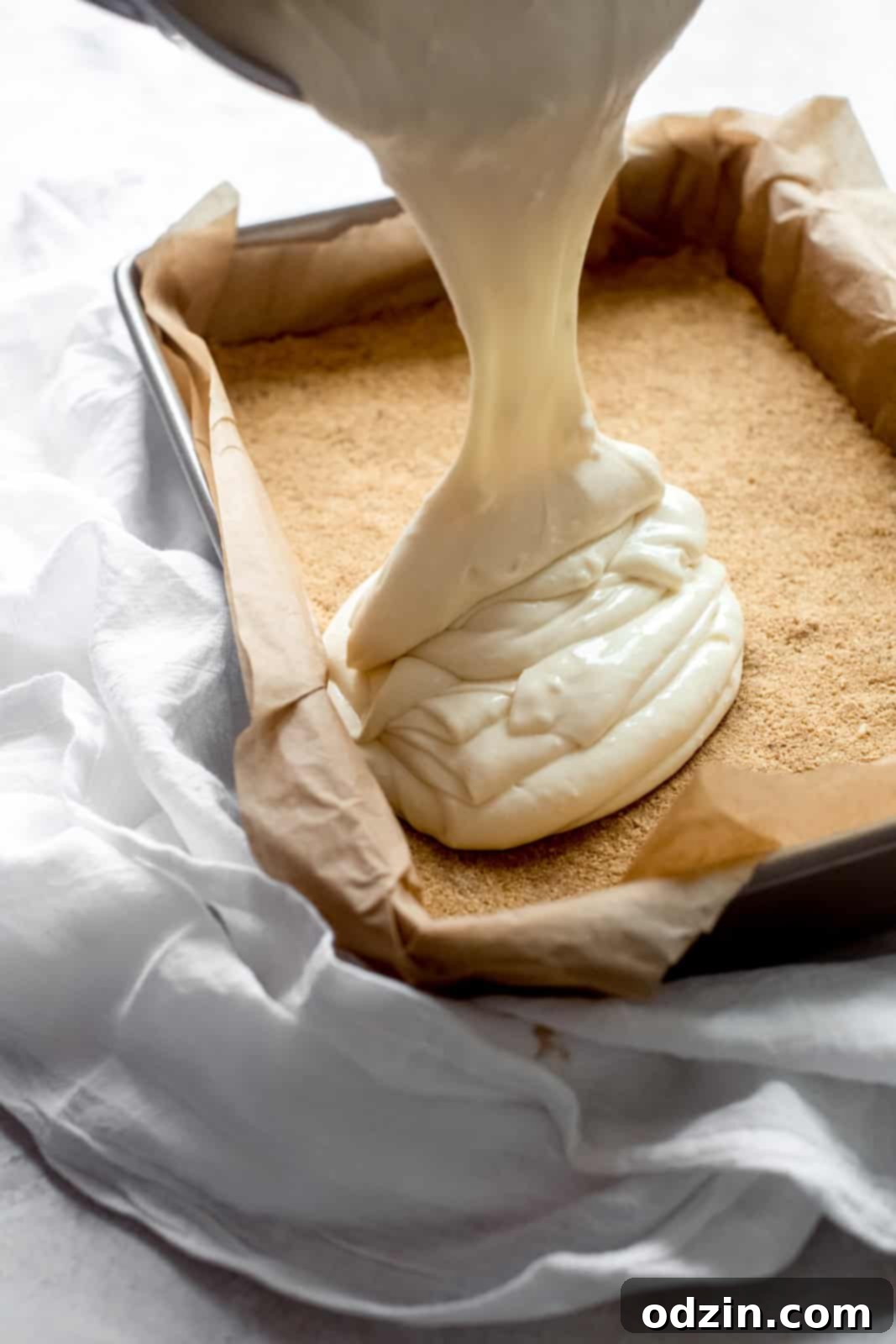 Pouring the smooth cheesecake mixture over the prepared graham cracker crust in a baking pan