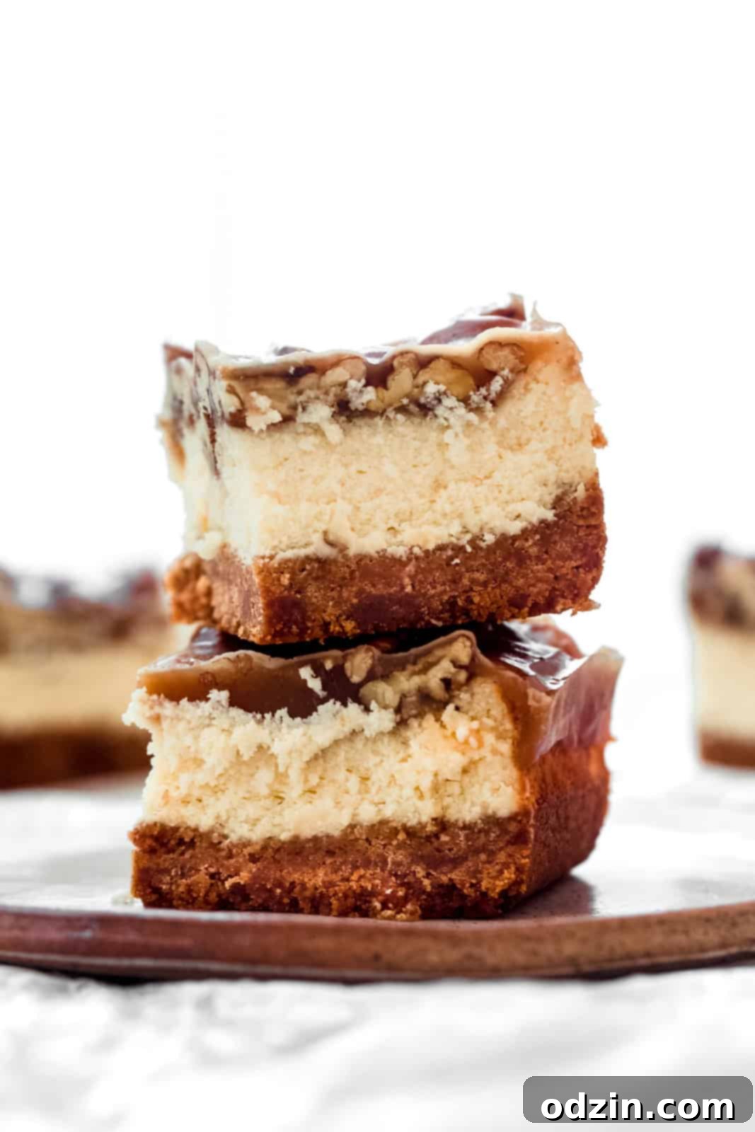 Two perfectly sliced pecan pie cheesecake bars stacked on a white plate, ready for serving