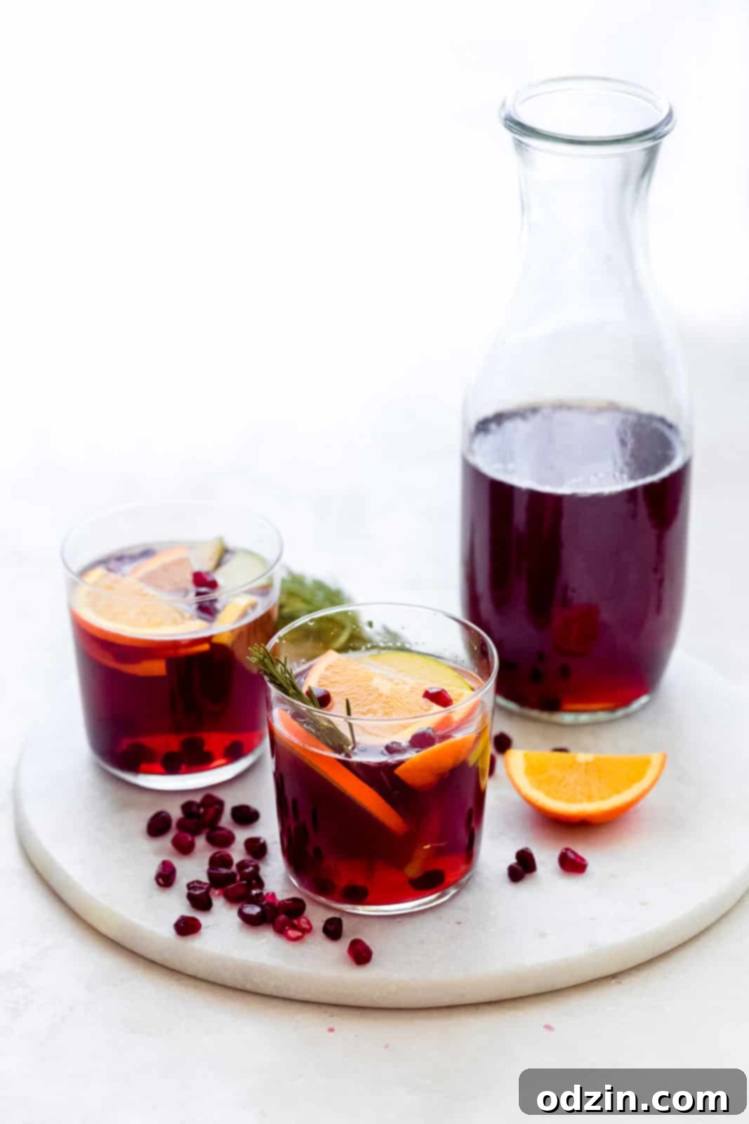mocktail in glasses on marble surface with oranges, apples, pomegranate arils, and rosemary in glass
