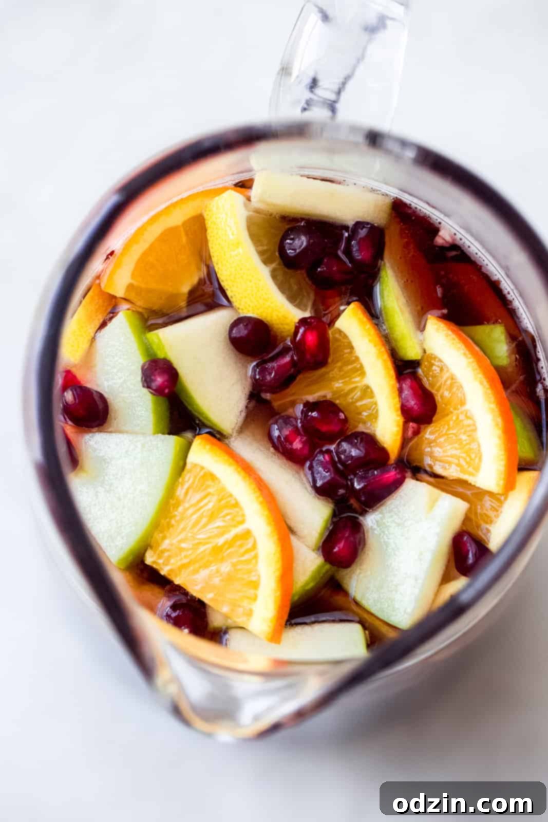 pitcher with sangria cocktail and various fruit slices and pomegranate arils