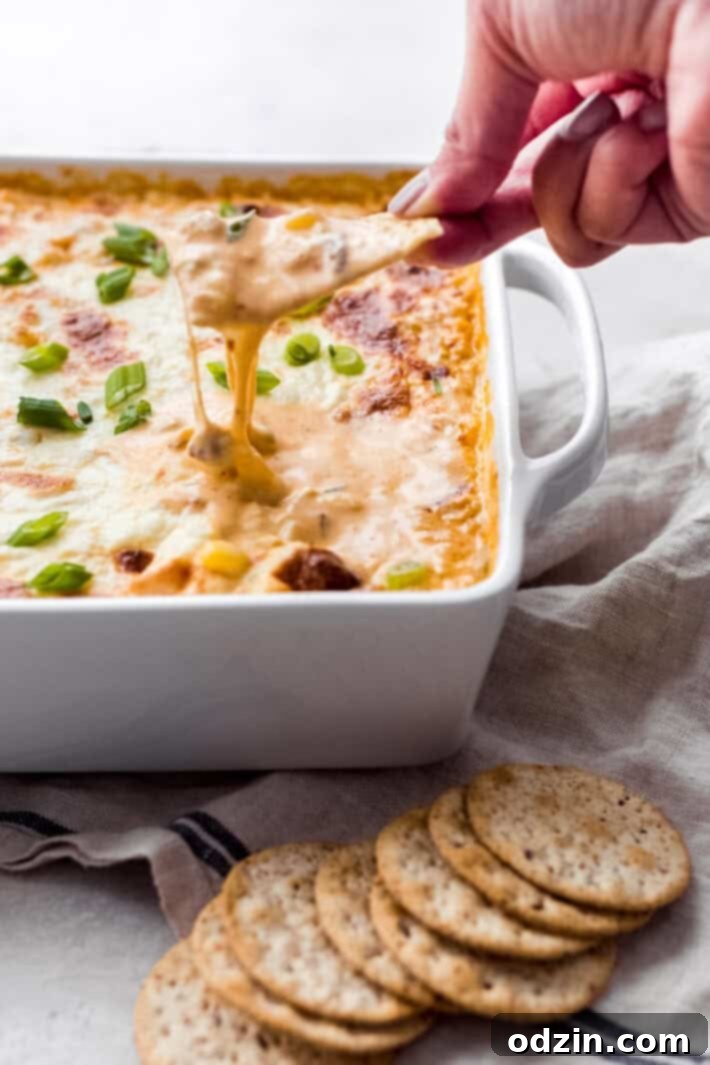 hand lifting hot chipotle shrimp and corn dip with tortilla chip