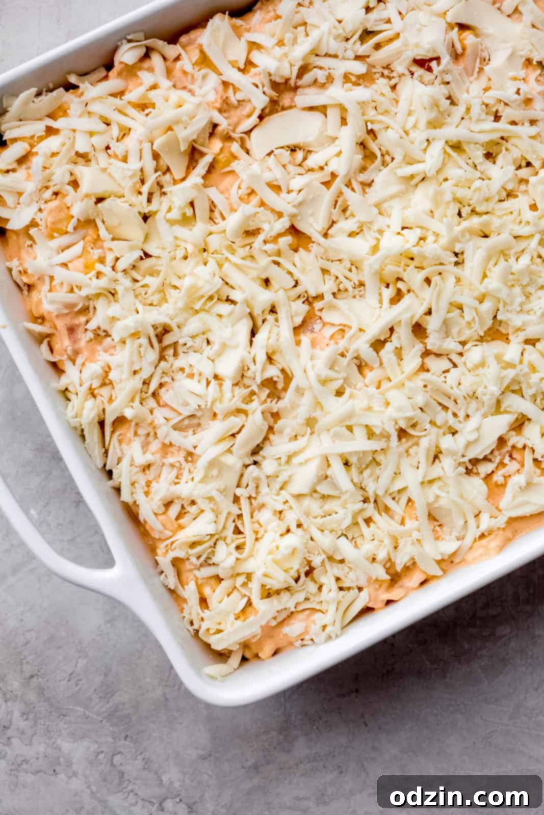 unbaked chipotle shrimp corn dip in white baking dish, topped with shredded Oaxaca cheese