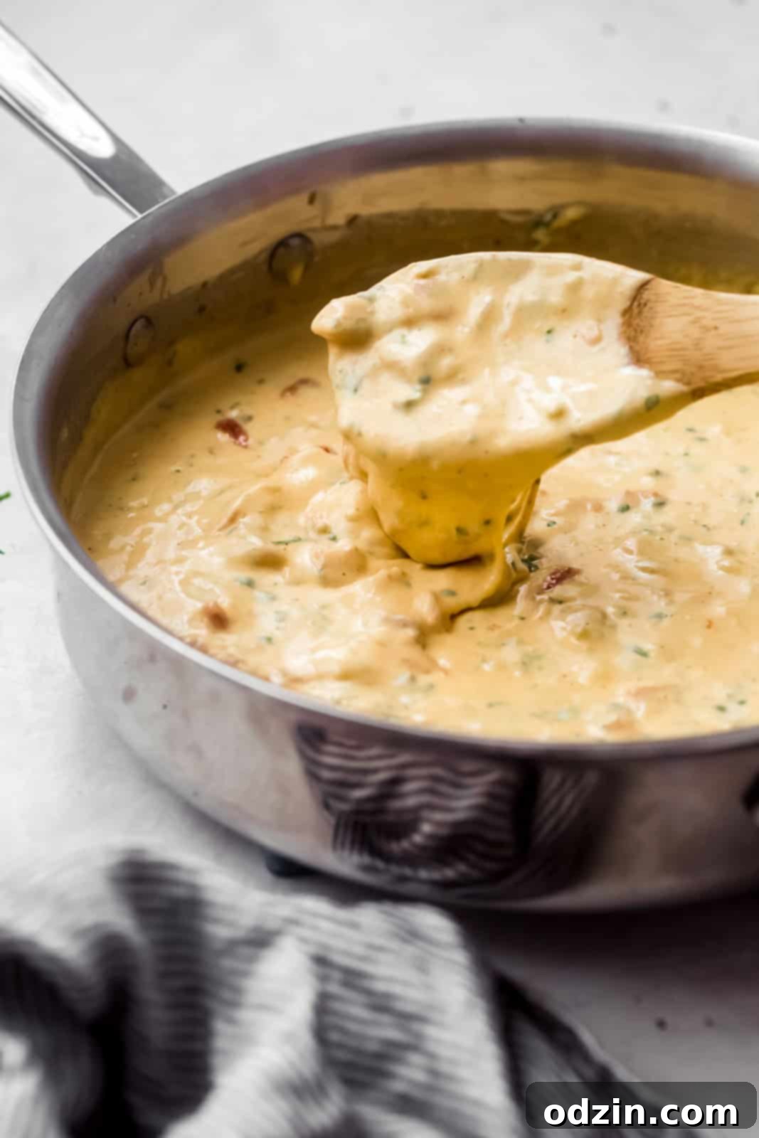 Zesty Texas Green Chili Queso 7 queso in saucepan cascading from wooden spoon