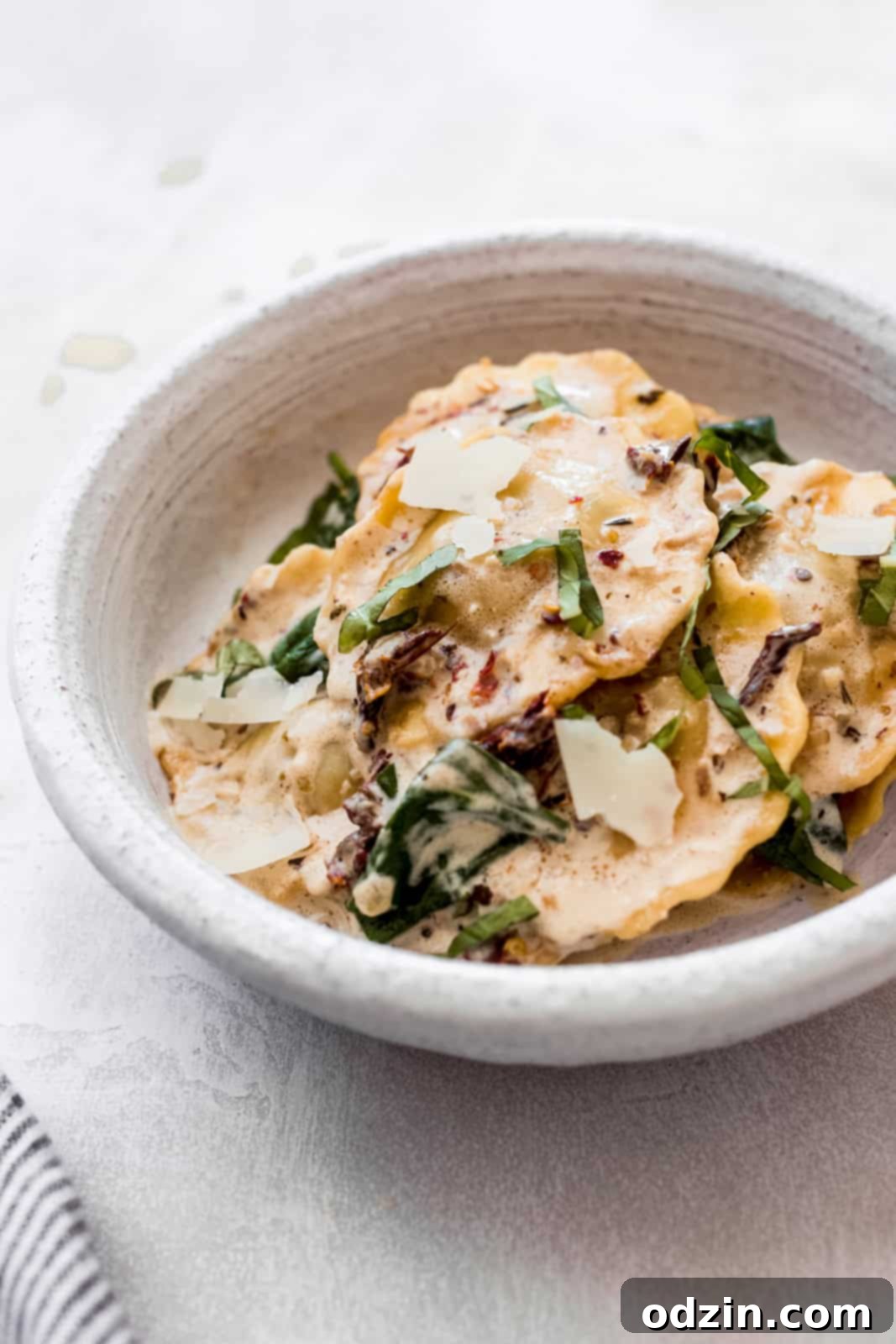 Creamy Tuscan Ravioli For An Unforgettable Date Night 6 side shot of ravioli in sauce in a bowl with parmesan and fresh basil