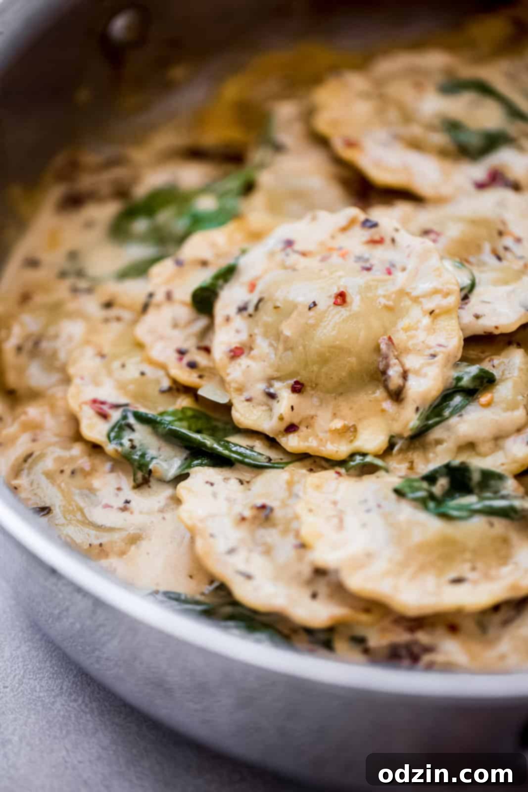 Creamy Tuscan Ravioli For An Unforgettable Date Night 7 ravioli in sauce in a skillet on grey surface