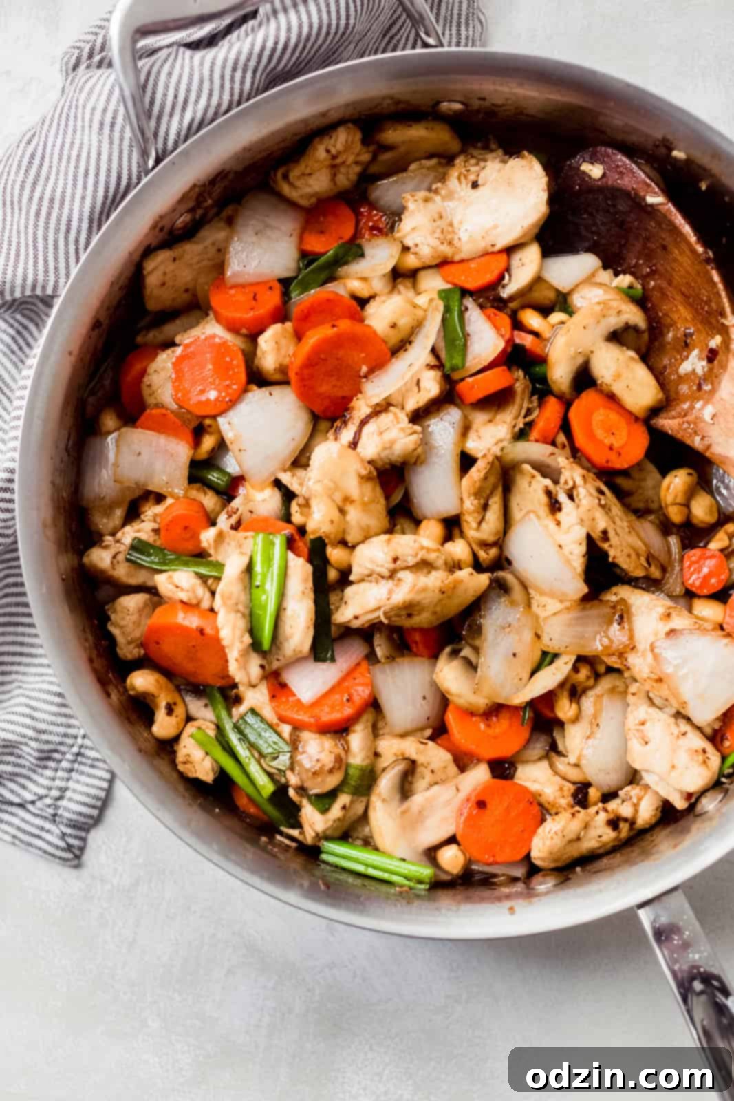 Effortless Thai Cashew Chicken That Outshines Takeout 2 Sizzling Thai cashew chicken stir-fry in a stainless steel pan with a wooden spoon, ready to be served.