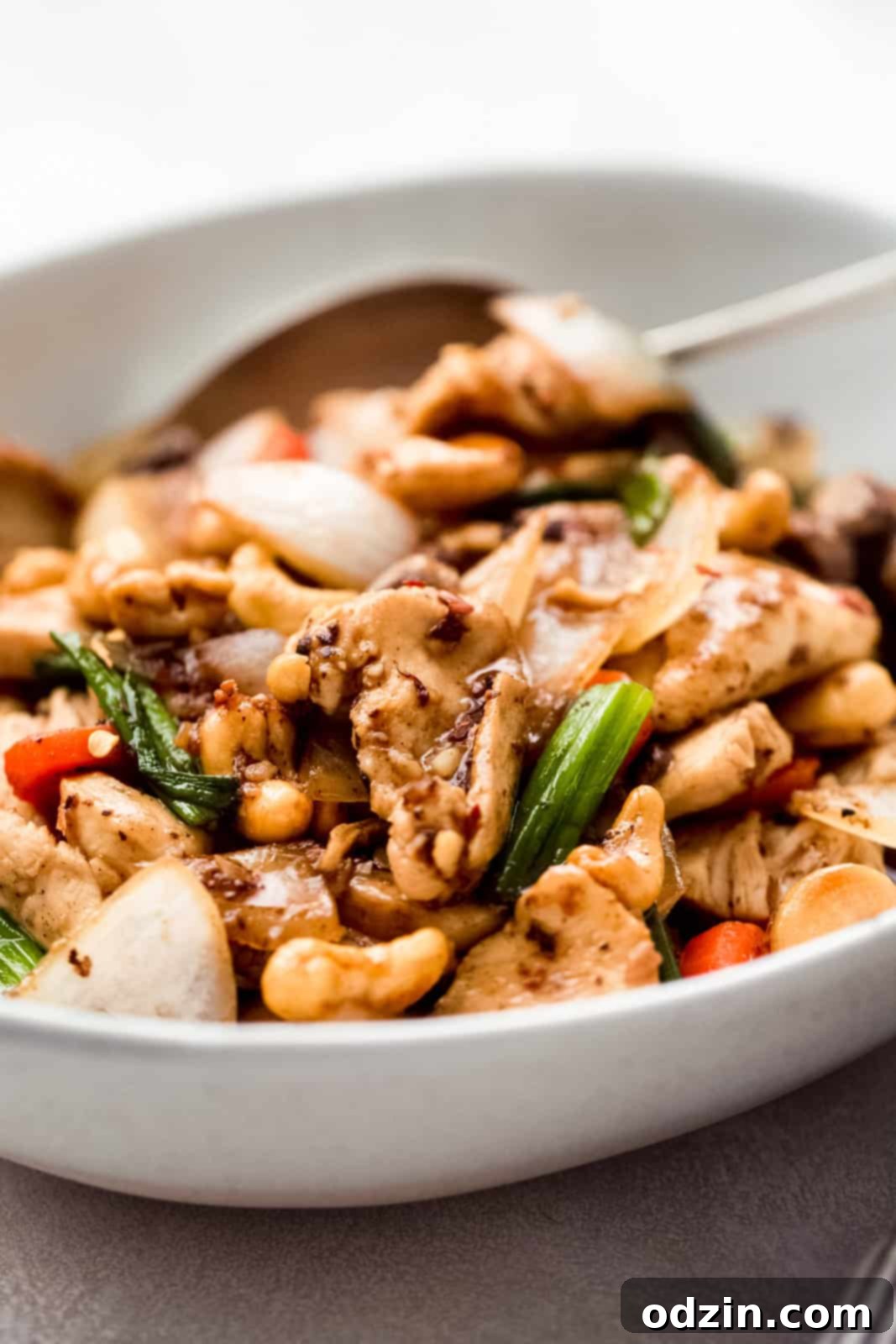 Effortless Thai Cashew Chicken That Outshines Takeout 3 Close-up of caramelized chicken pieces with fresh scallions, sliced onions, and vibrant carrots, artfully arranged in a white serving dish.