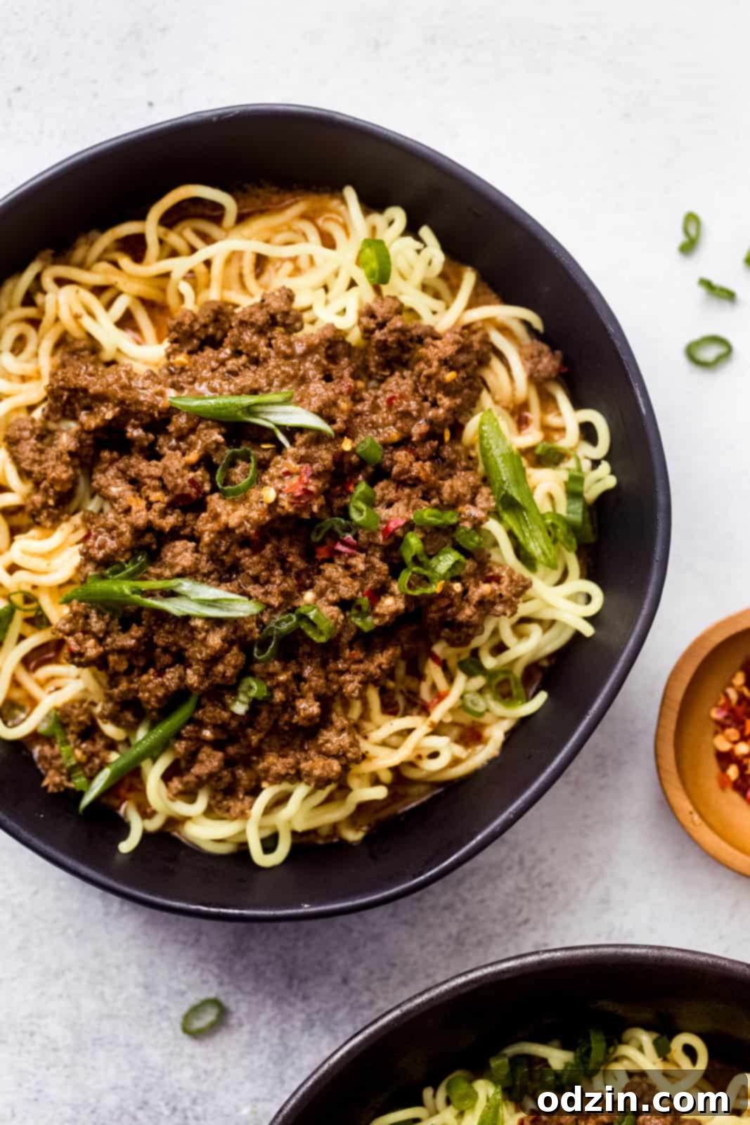 dan dan noodles in black bowl topped with scallions