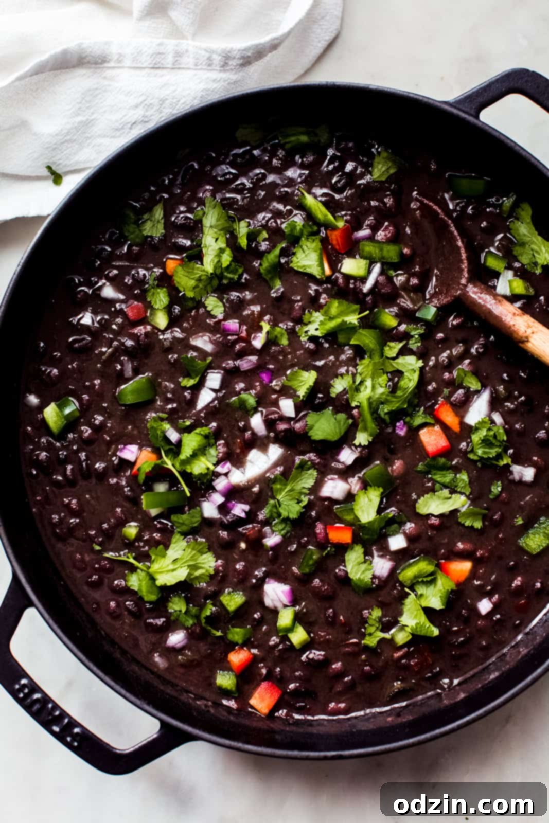  cuban black bean soup in cast iron pot topped with onions cilantro and peppers