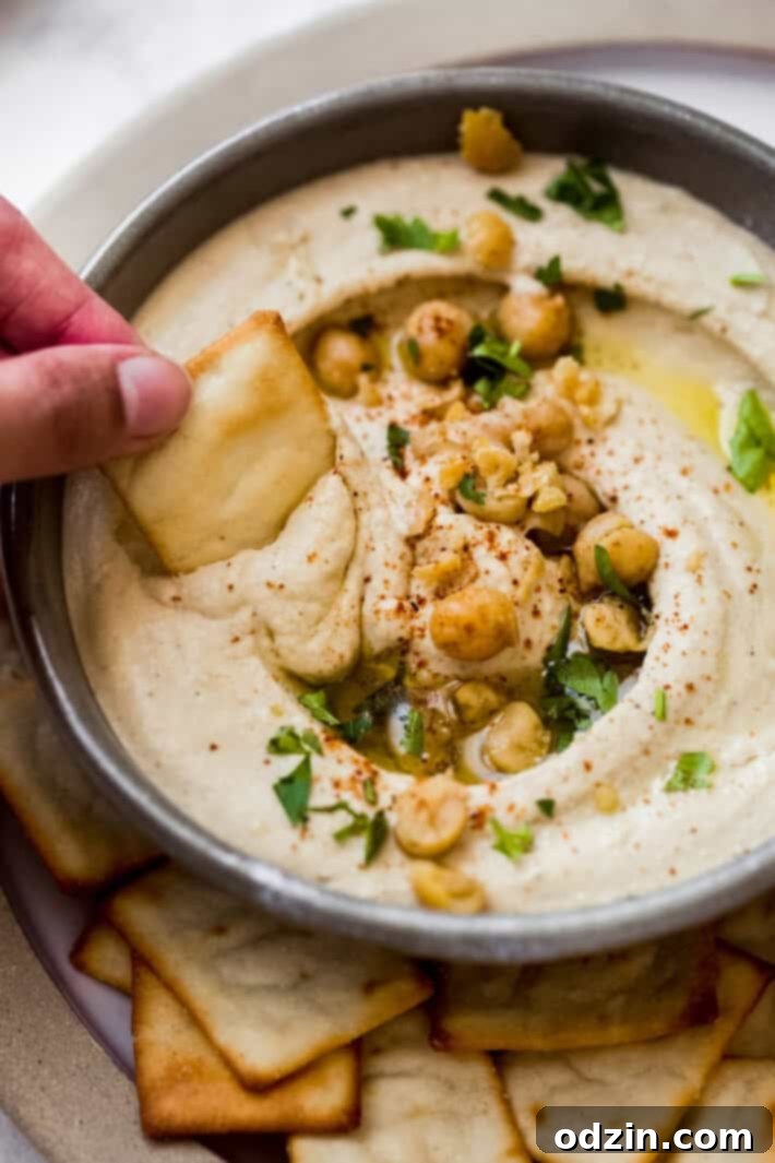 pita chip dipped in homemade hummus A close-up of a pita chip generously dipped into a bowl of homemade hummus, showing off its rich, smooth texture.