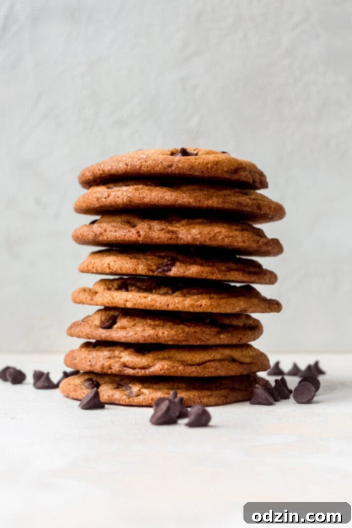 Ultimate Chewy Chocolate Chip Cookies 6 A perfectly stacked pile of freshly baked chocolate chip cookies with loose chocolate chips scattered around.