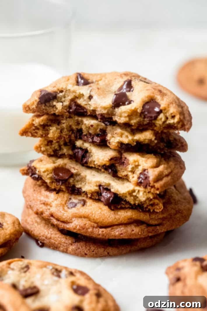 Ultimate Chewy Chocolate Chip Cookies 7 A stack of golden-brown chocolate chip cookies, with some broken in half to reveal their soft, chewy interior texture, resting on a marble surface.