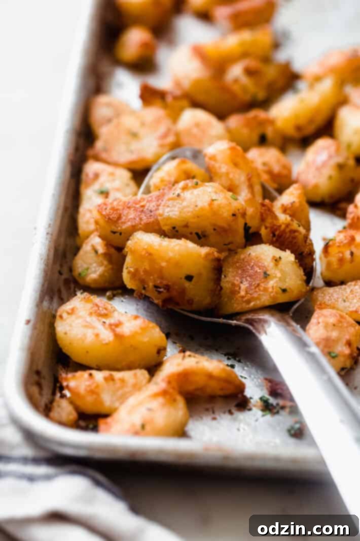 Crispy Garlic Oven Potatoes 2 crispy roasted potatoes on a metal spoon resting on sheet pan