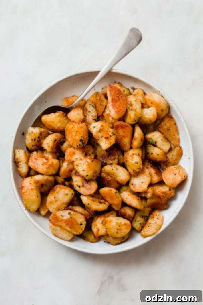 Crispy Garlic Oven Potatoes 3 roasted potatoes speckled with fresh parsley in a white speckled bowl with metal spoon