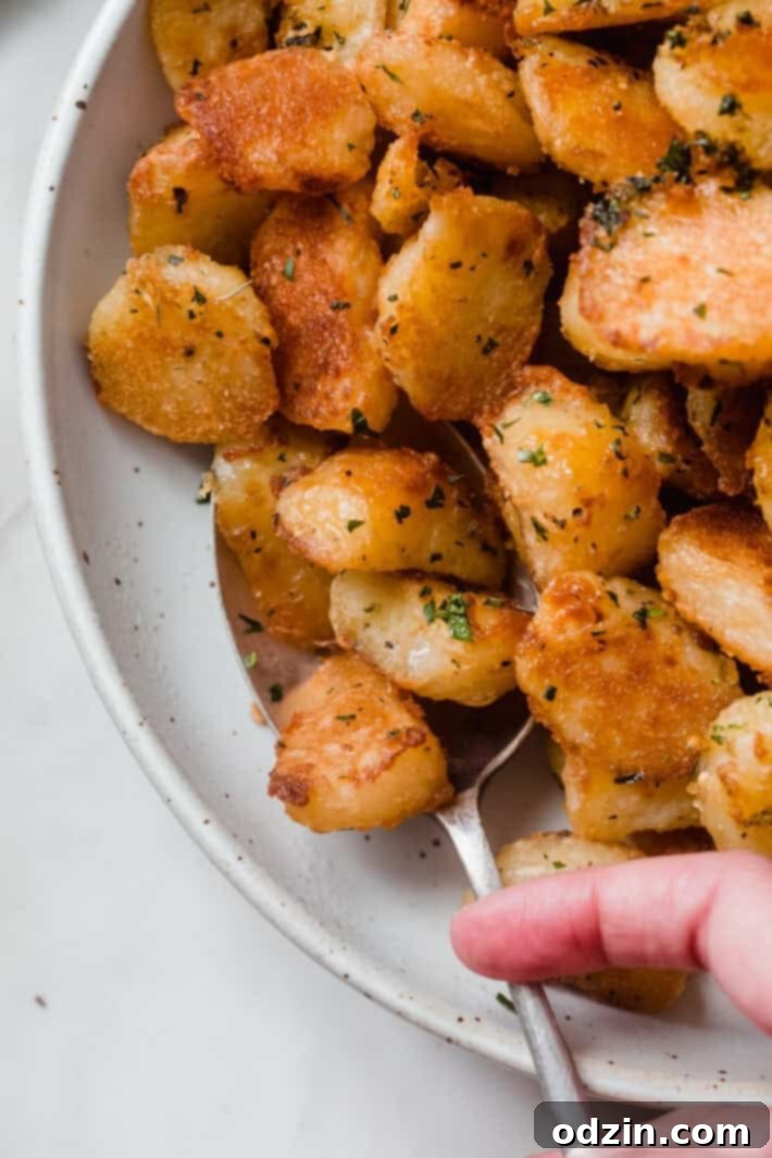 Crispy Garlic Oven Potatoes 7 close up of roasted potato texture in bowl with hand holding spoon