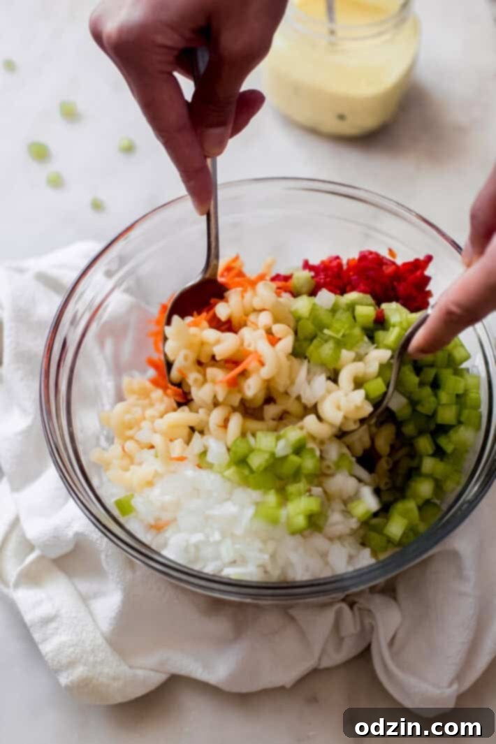 Crave-Worthy Macaroni Salad 6 hands tossing cold pasta salad with vegetables