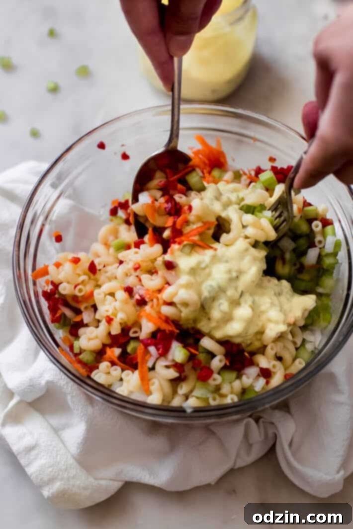 Crave-Worthy Macaroni Salad 8 hands tossing prepared cold pasta salad with spoon and fork