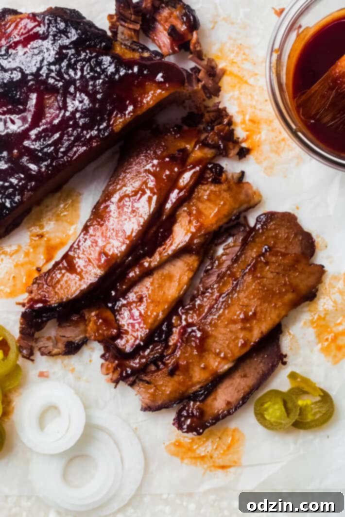 sliced bbq beef brisket on crinkled wax paper with sliced onions, pickled jalapeños and bbq sauce