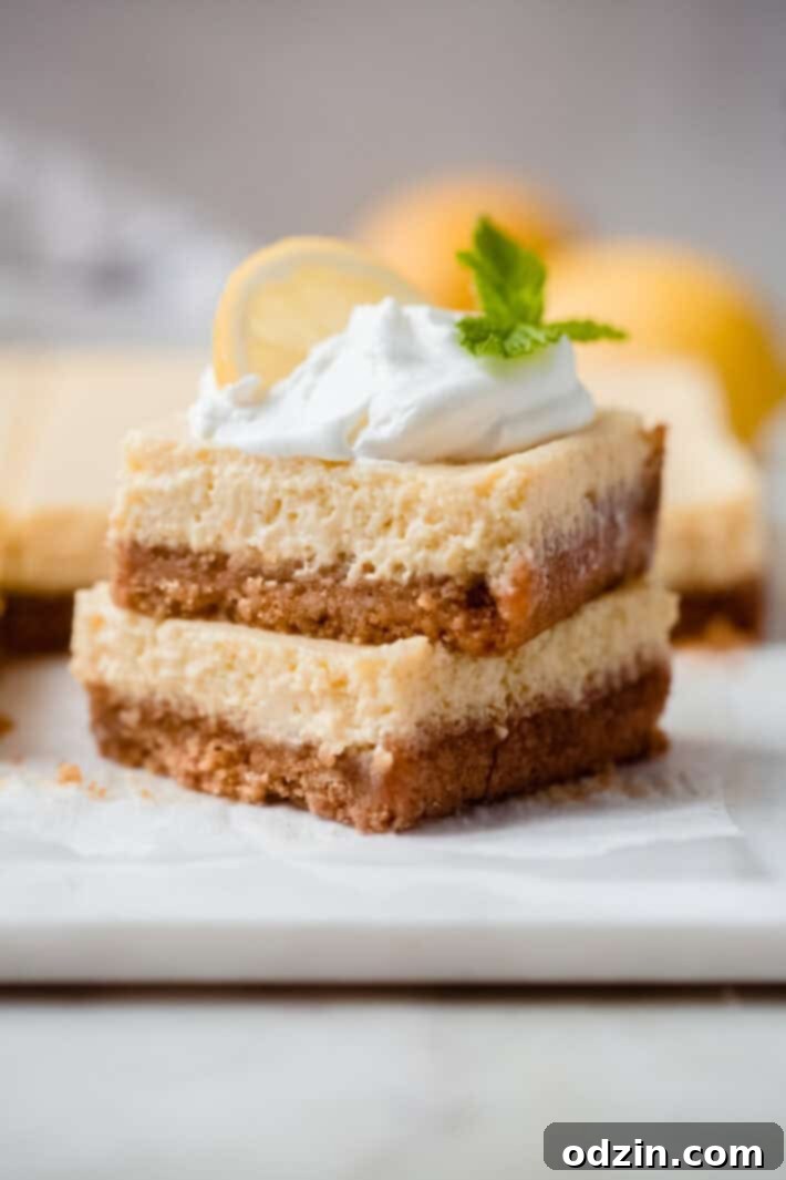 stack of two creamy lemon squared topped with whipped cream, a lemon slice, and a sprig of mint