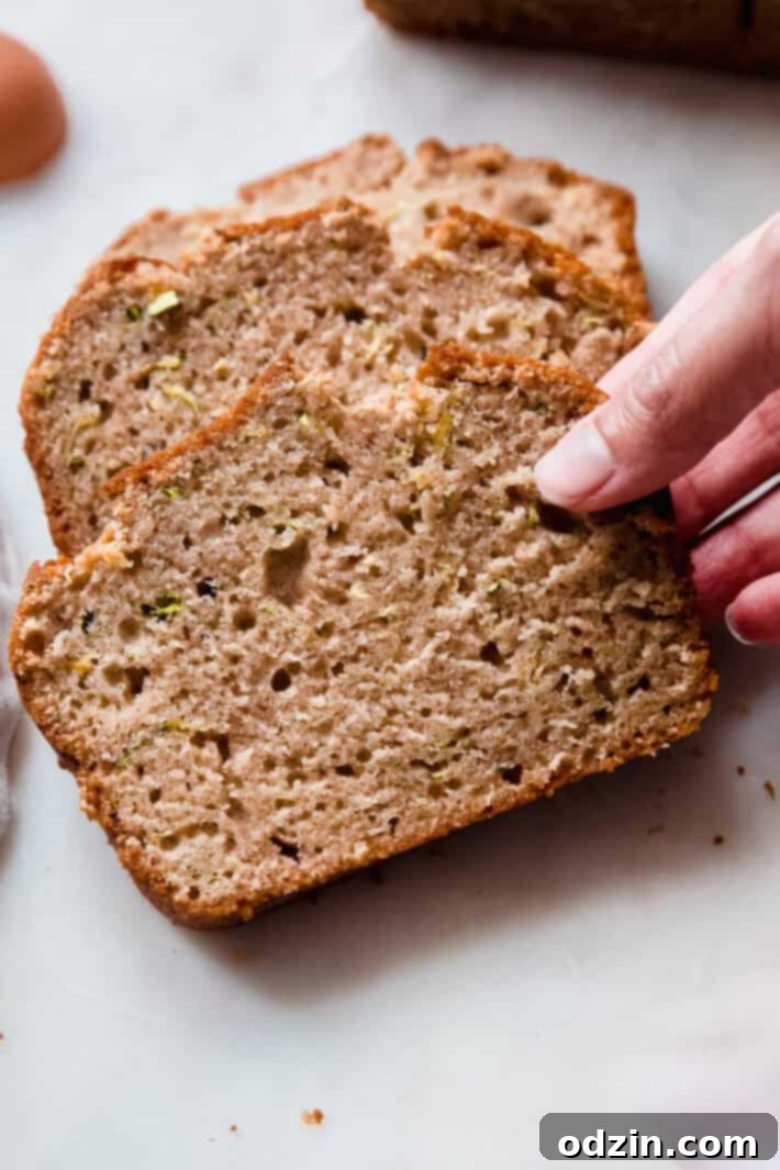 A hand reaching for a slice of freshly baked zucchini bread from a white marble surface, inviting a taste.