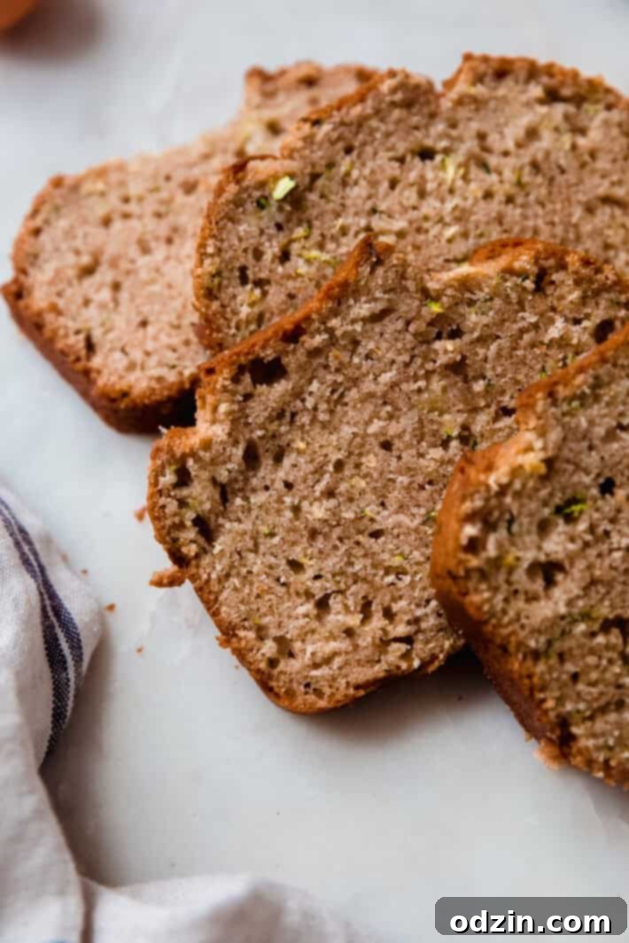 Close-up view of several slices of zucchini bread on white marble, revealing the moist texture and grated zucchini speckles.