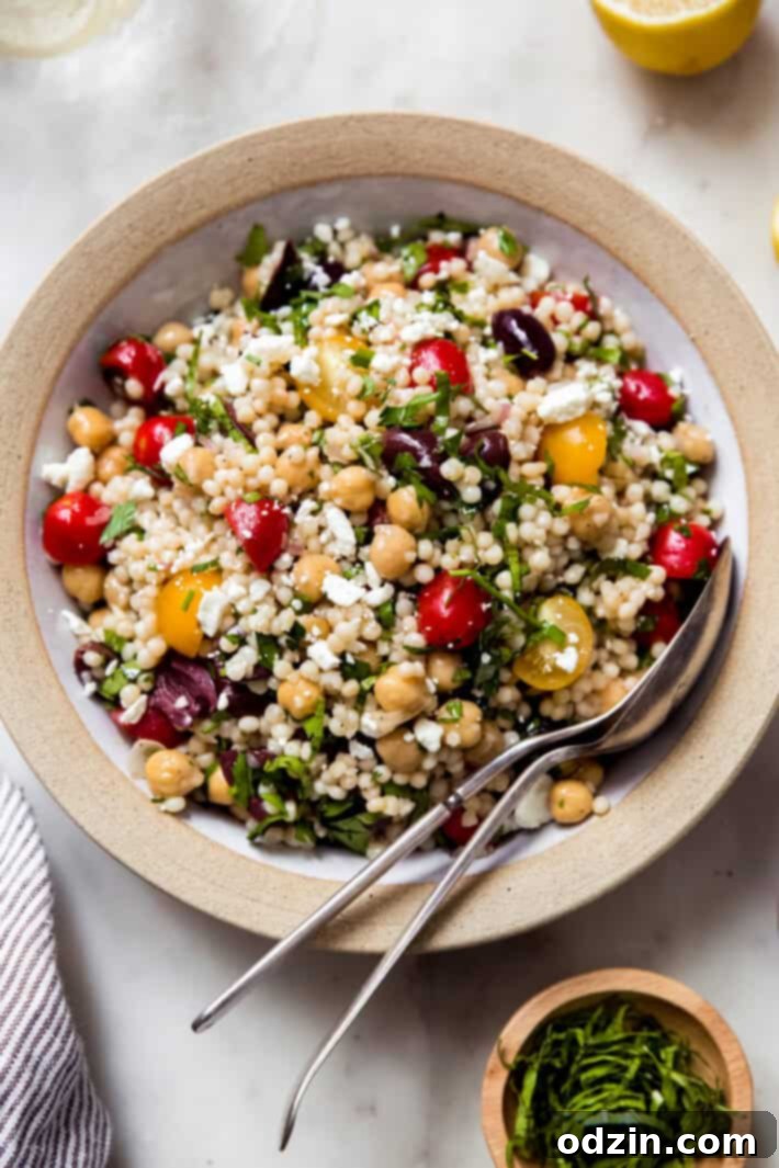 prepared Israeli couscous chickpea salad in rimmed bowl with spoon and fork