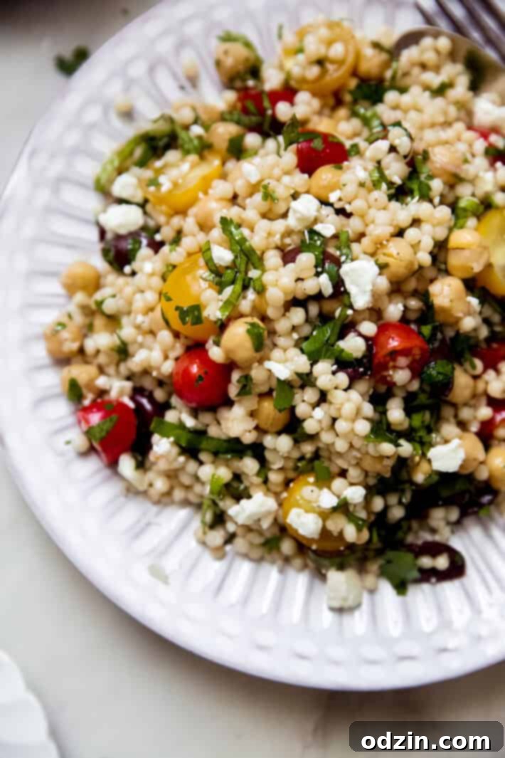 fluted plate with a close up of Israeli couscous salad with feta cheese and fresh tomatoes