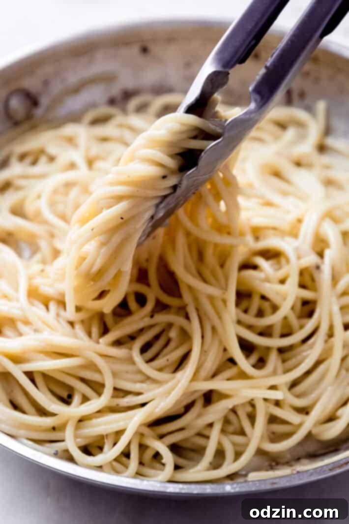 tongs holding cheese and pepper sauce coated spaghetti in skillet