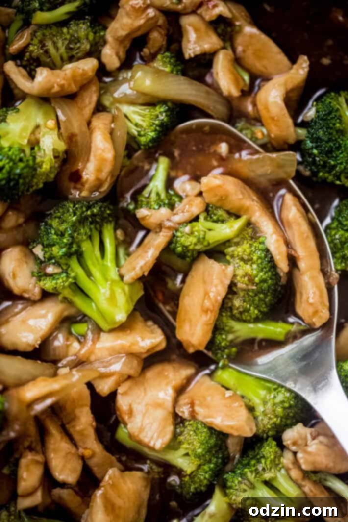 metal spoon holding prepared stir fry in skillet showing chicken, broccoli, and sauce