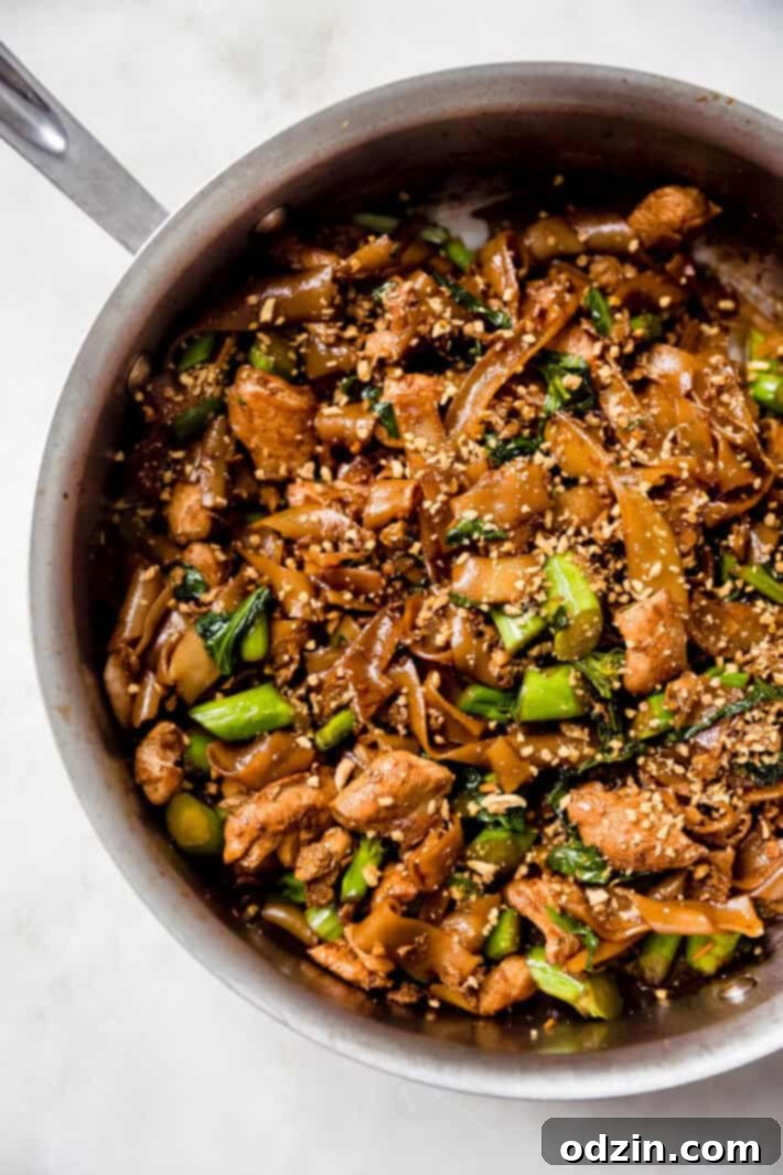 Sizzling skillet with freshly prepared Pad See Ew topped with crispy fried garlic, ready to serve.