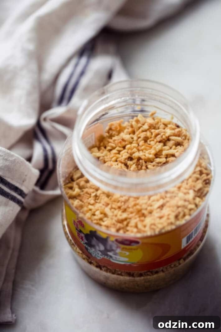 Close-up of a plastic jar filled with crispy, golden fried garlic, a key condiment for Thai dishes.