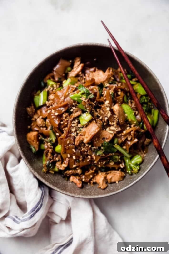 A vibrant green bowl filled with perfectly cooked Pad See Ew, chopsticks resting gracefully on the rim.