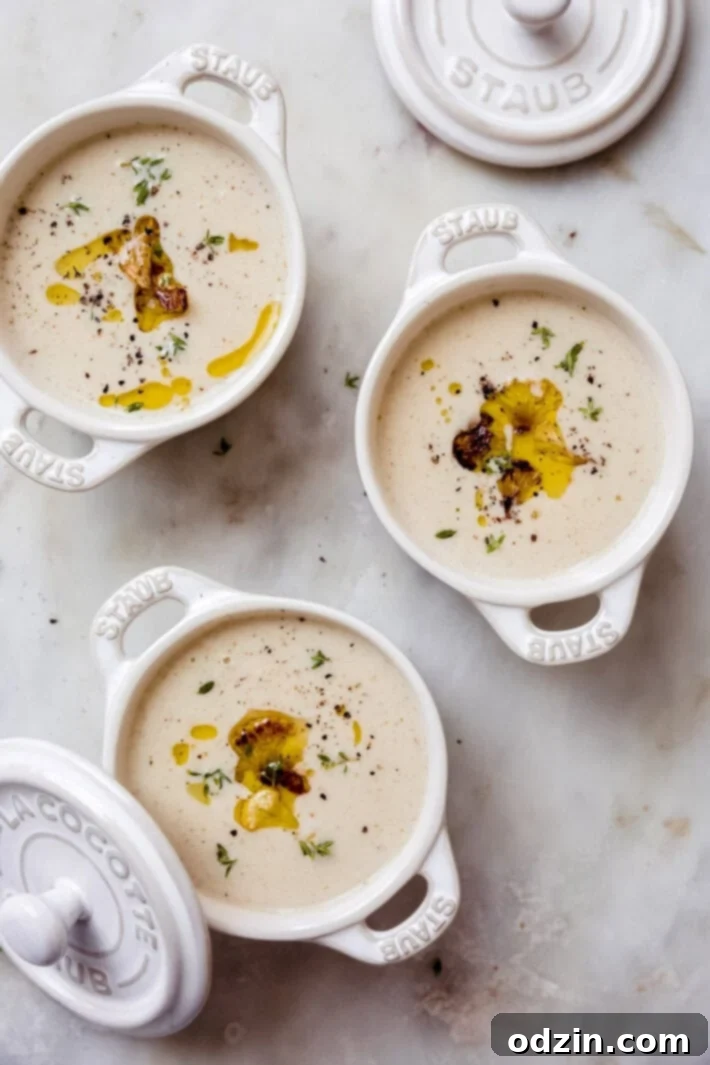 Velvet Truffle Cauliflower Dream 3 Three small, elegant white bowls with handles, filled with delicious and creamy roasted cauliflower soup.