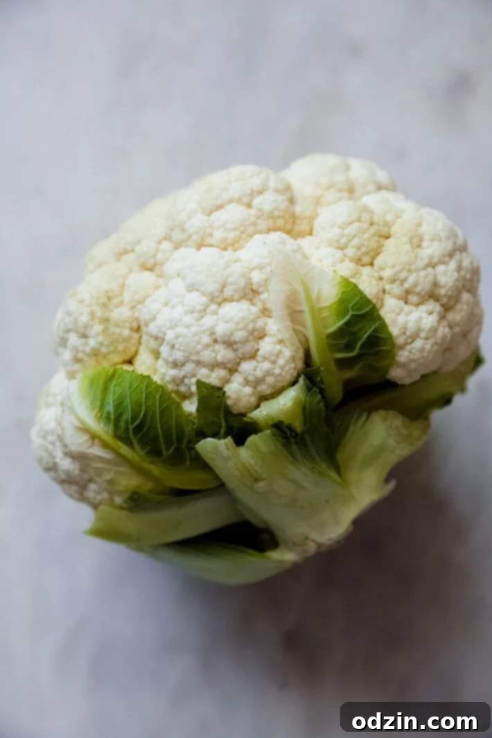 Velvet Truffle Cauliflower Dream 4 A fresh, vibrant head of cauliflower resting on a clean white marble surface, ready for preparation.