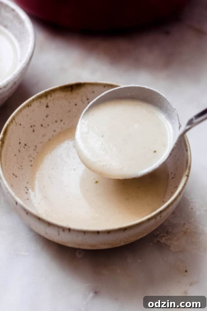 Velvet Truffle Cauliflower Dream 7 A wooden ladle carefully pouring the smooth and creamy roasted cauliflower soup into a beautiful speckled serving bowl.