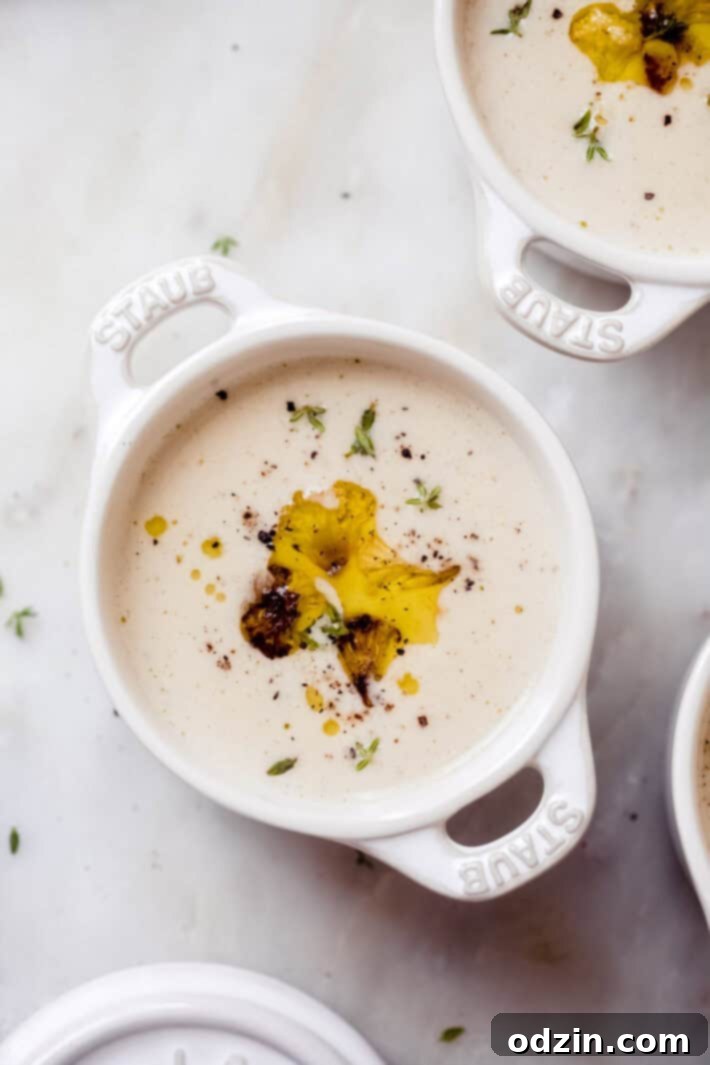 Velvet Truffle Cauliflower Dream 8 Close-up of a small, rustic soup bowl with handles, brimming with creamy cauliflower soup, adorned with roasted cauliflower florets, fresh thyme leaves, and a delicate swirl of truffle oil.