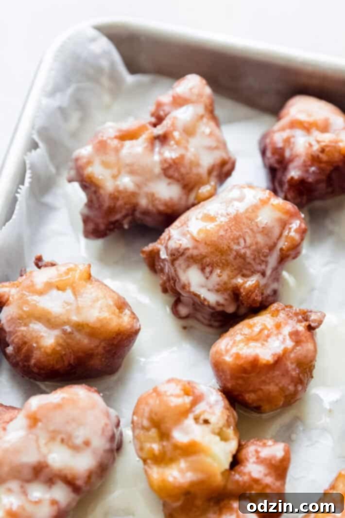 Effortless Maple Honeycrisp Apple Fritters 2 maple-glazed apple fritters on baking sheet lined with wax paper